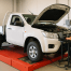 Mechanic tuning a white work ute on a dynamometer in a bright workshop.